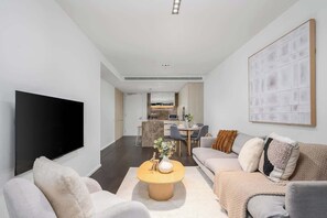 Un salon moderne avec un téléviseur à écran plat, une table basse, des canapés et, au fond, un coin repas.