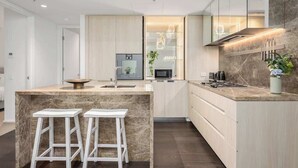 Una cocina moderna con una isla de mármol, taburetes blancos y un microondas empotrado.