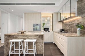 Una cocina moderna con una isla de mármol, taburetes blancos y un microondas empotrado.