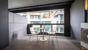 Un balcón moderno con una mesa redonda y dos sillas, ventanas amplias y un equipo de aire acondicionado a la vista.