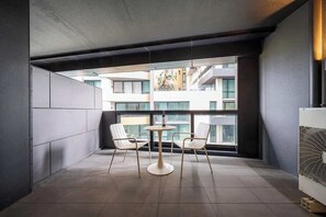 Un balcón moderno con una mesa redonda y dos sillas, ventanas amplias y un equipo de aire acondicionado a la vista.