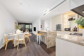 Een moderne keuken met een marmeren eiland, een eetgedeelte met witte stoelen en een groot raam.