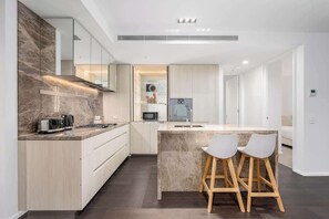 A modern kitchen with a central island, bar stools, and a microwave. - LaneStay - Grand Prix Retreat w Pool, Gym, Parking (Melbourne)