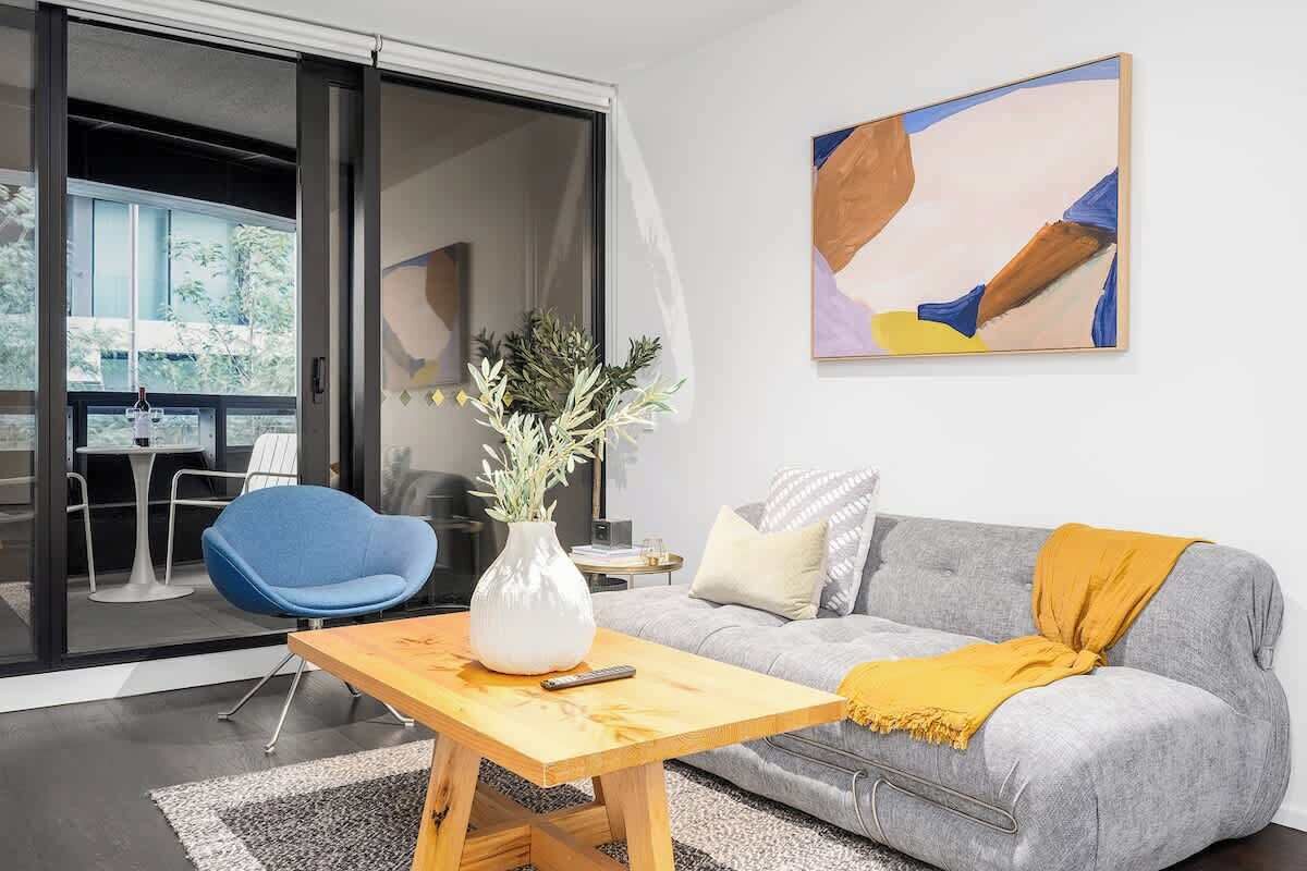 Un salon moderne avec un canapé gris, un fauteuil bleu, une table basse en bois et un tableau accroché au mur.