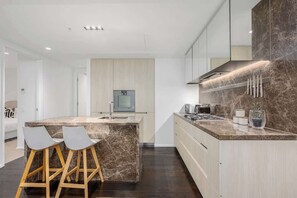 A modern kitchen with a marble island, bar stools, a microwave, and a built-in oven. - LaneStay - 2B2B Resort Living, Pool Gym Parking (Melbourne)