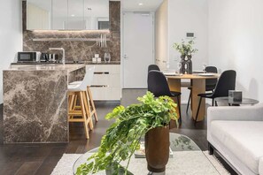 A modern kitchen with a marble island, a dining area with a wooden table and chairs, and a living area with a sofa and a plant. - LaneStay - 2B2B Resort Living, Pool Gym Parking (Melbourne)