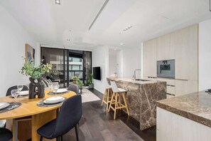 A modern kitchen with a marble island, a dining area with a wooden table and chairs, and a living area with a sofa and a TV. - LaneStay - 2B2B Resort Living, Pool Gym Parking (Melbourne)