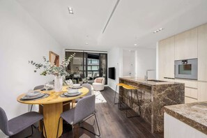A modern kitchen with a marble island, a dining area with a wooden table and chairs, and a living space with a sofa and a TV. - LaneStay - Contemporary Living, Pool, Gym, Parking (Melbourne)