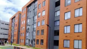 A multi-story residential building with a brick facade, multiple windows, and a green outdoor area with a paved walkway. - Cozy apartment ideal for travelers, digital nomads, or families. (Bogotá)