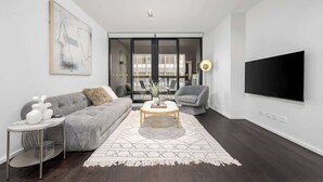 Ein modernes Wohnzimmer mit grauem Sofa, Couchtisch, Fernseher und einem großen Fenster.
