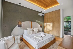 Ein modernes Schlafzimmer mit einem großen Bett, zwei Pendelleuchten, einer Holzbalkendecke und Blick auf Grünflächen.