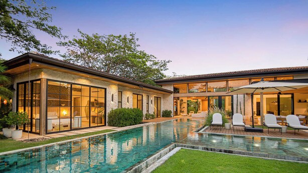 Une maison moderne dotée d’une piscine, de grandes fenêtres et d’un espace salon extérieur.