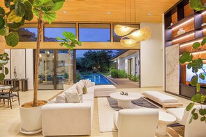 A modern interior with a pool, white furniture, and a large window overlooking the outdoors. - Casa Kaikoo (Hacienda Pinilla)