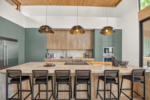 A modern kitchen with a central island, bar stools, and pendant lighting. - Casa Kaikoo (Hacienda Pinilla)