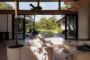 Ein modernes Wohnzimmer mit einer Couch, einem Couchtisch und einem großen Fenster mit Blick auf einen Garten.