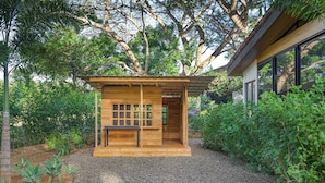 Une cabane en bois avec une fenêtre et une porte, entourée d’un chemin de gravier et de verdure.