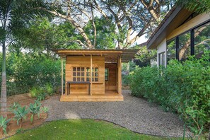 A wooden cabin with a window and a door, surrounded by a gravel path and greenery. - Casa Kaikoo (Hacienda Pinilla)
