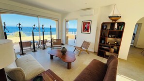 A spacious living room with a large window overlooking the sea, a wooden coffee table, a bookshelf, and a comfortable sofa. - Exceptional Marine de Davia villa facing the sea and close to the beaches (Corbara)