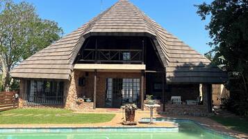 A house with a swimming pool, stone walls, and a large window.