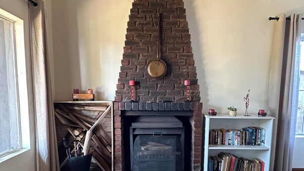 A room with a brick fireplace, a bookshelf, a patterned rug, and a window. - Kariki Villa with Panoramic Valley Views (Outer West Durban)