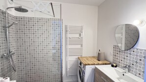 Un baño moderno con cabina de ducha de vidrio, lavadora integrada, tocador de madera y un espejo grande.