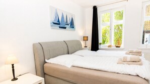 Quarto com cama, mesa de cabeceira, luminária, janela com cortinas e um quadro na parede.