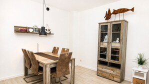 Uma área de refeições com mesa e cadeiras de madeira, um lustre pendurado e um armário com portas de vidro.