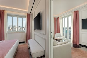 A hotel room with a bed, a bench, a sofa, a TV, and a balcony with curtains.