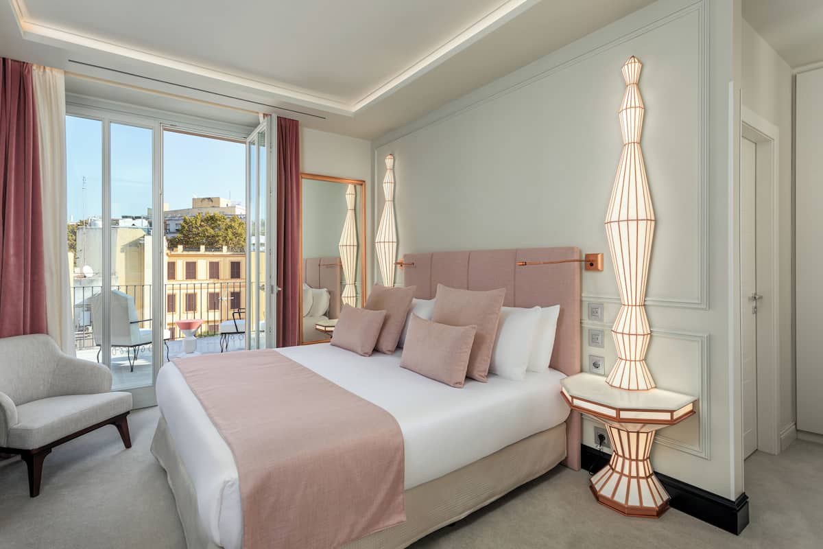 Habitación de hotel con una cama grande, una zona de estar y vistas a la ciudad a través de amplias ventanas.