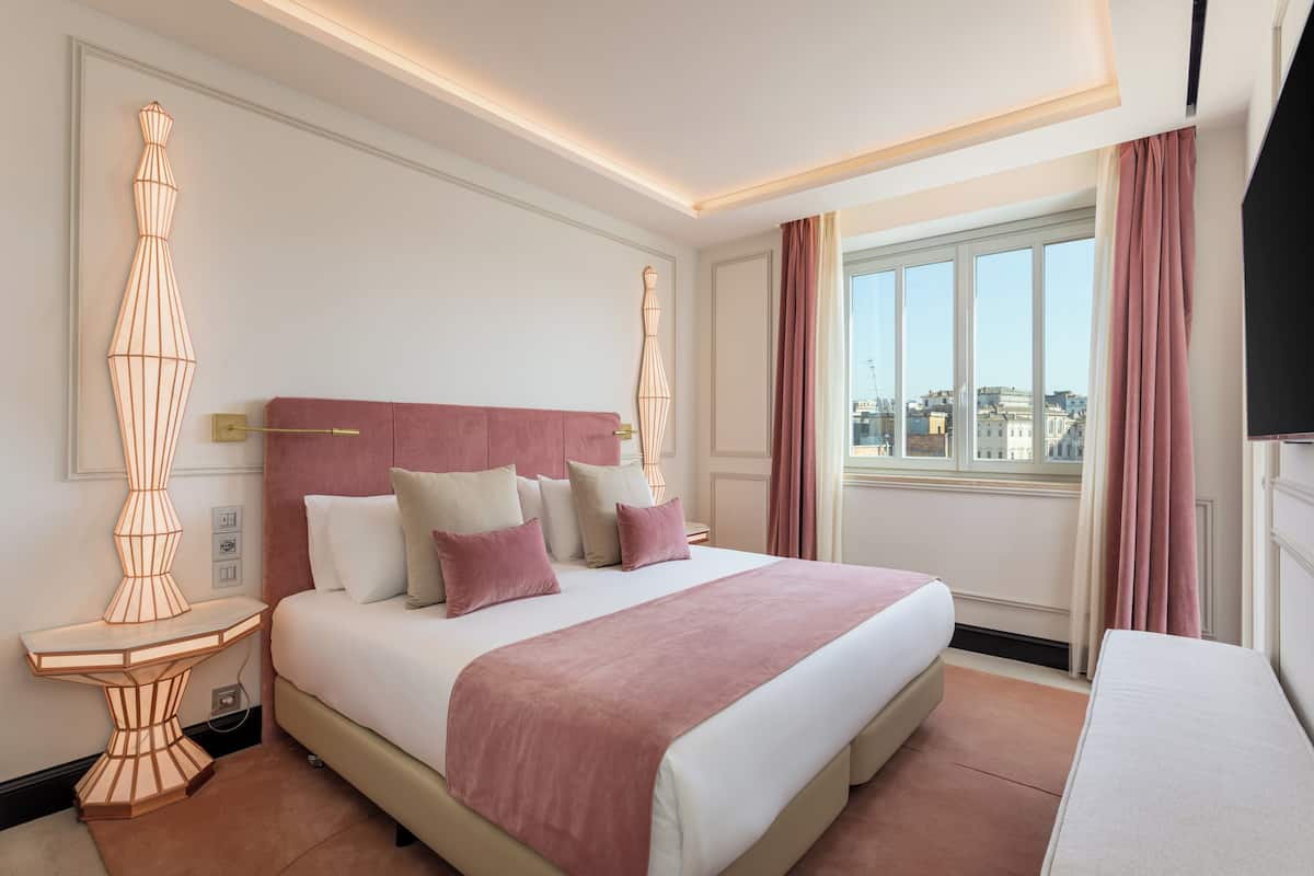 Un hotel moderno con una cama grande, una mesita de noche, una lámpara de pie decorativa y vistas a la ciudad desde la ventana.