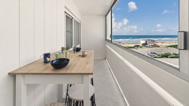 En balkon med et træbord, stole og udsigt til stranden og havet.