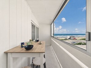 Un balcón con mesa y sillas de madera, y vista a la playa y al océano.