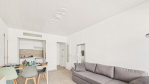En moderne stue med en grå sofa, et spisebord med stole, og et køkken i baggrunden.