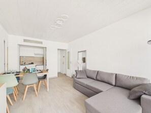 Ein modernes Wohnzimmer mit einem grauen Sofa, einem Esstisch mit Stühlen und einer Küche im Hintergrund.