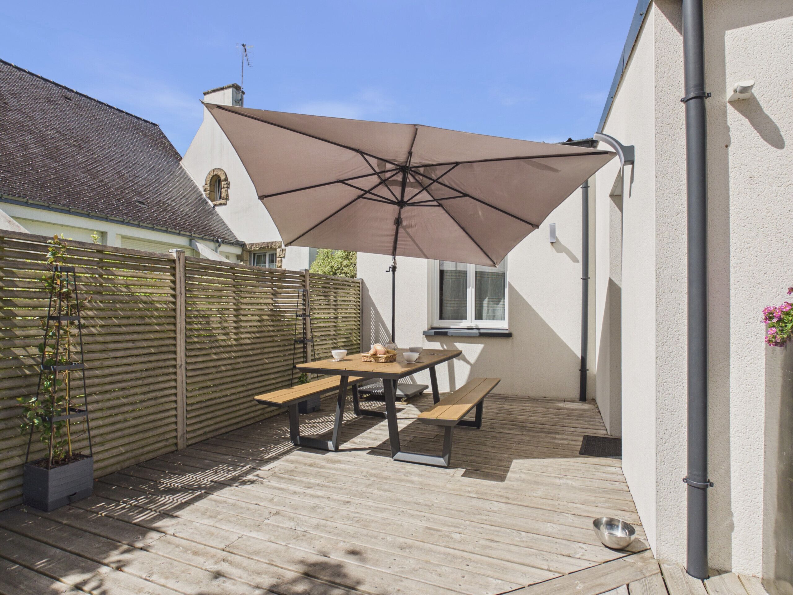 A wooden deck with a table and benches, a large umbrella, and a wooden fence.