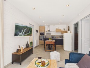 Eine moderne Küche mit integrierten Geräten, ein Essbereich mit Tisch und Stühlen sowie ein Wohnzimmer mit Sofa und Wand-Fernseher.
