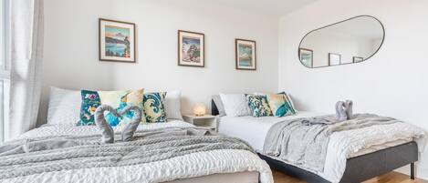 A bedroom with two beds, a bedside table with a lamp, and a large mirror on the wall.
