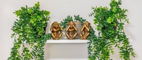 A white shelf with three golden Buddha statues flanked by green hanging plants.