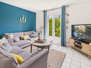 Ein modernes Wohnzimmer mit einer Couch, Couchtisch, Fernseher und Blick ins Grüne durch das Fenster.