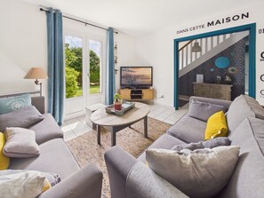 Ein Wohnzimmer mit Sofa, Couchtisch, Fernseher und einer Treppe, die in einen anderen Raum führt.