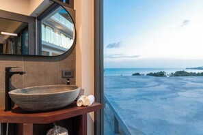 Ein Badezimmer mit einem großen, runden Waschbecken, einem Spiegel und Blick aufs Meer.