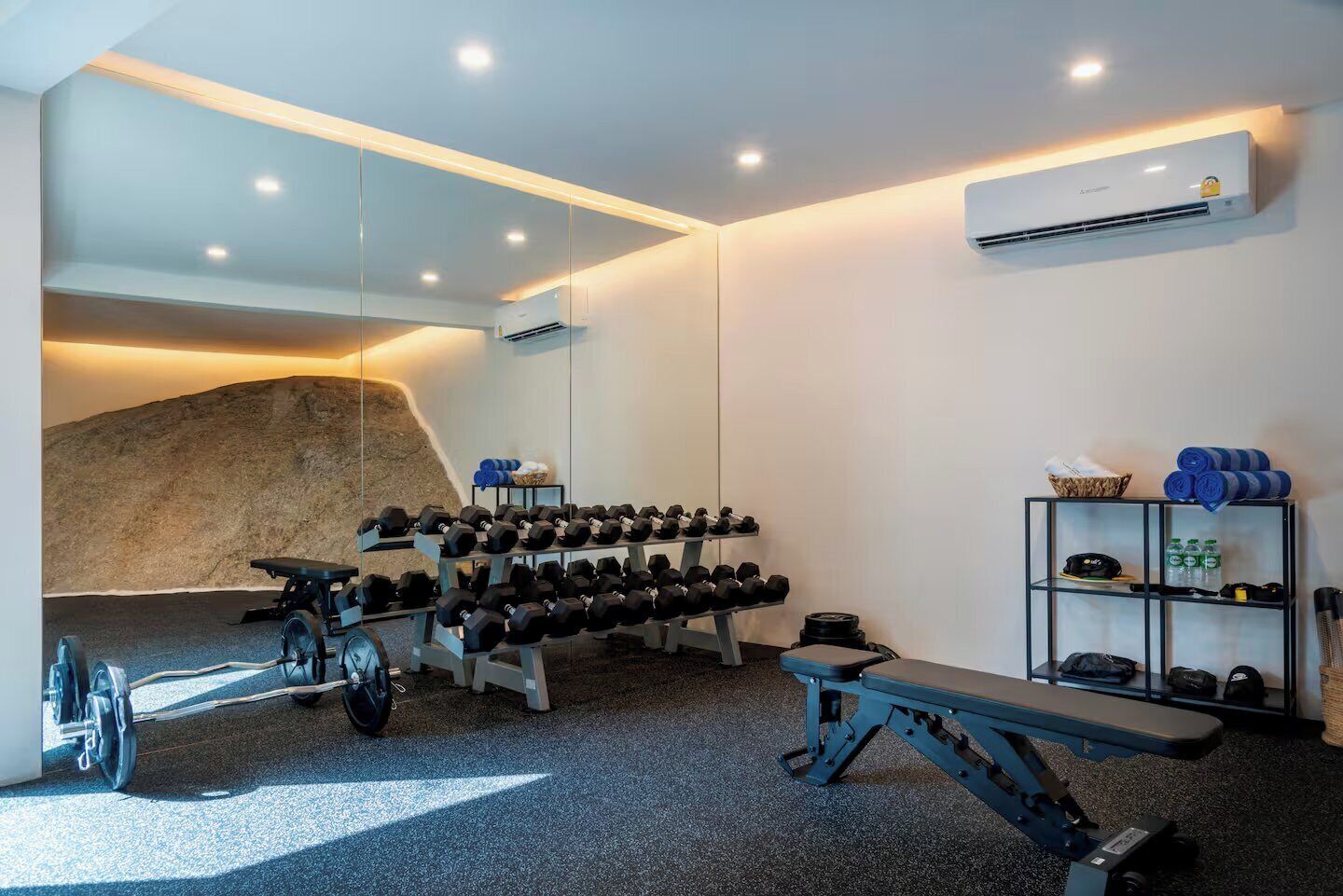 Un gimnasio con equipo de ejercicio, una banca y un aire acondicionado instalado en la pared.