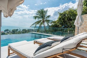 Ein Pool-Loungebereich mit zwei Liegestühlen, einer Palme und Blick auf den Ozean.