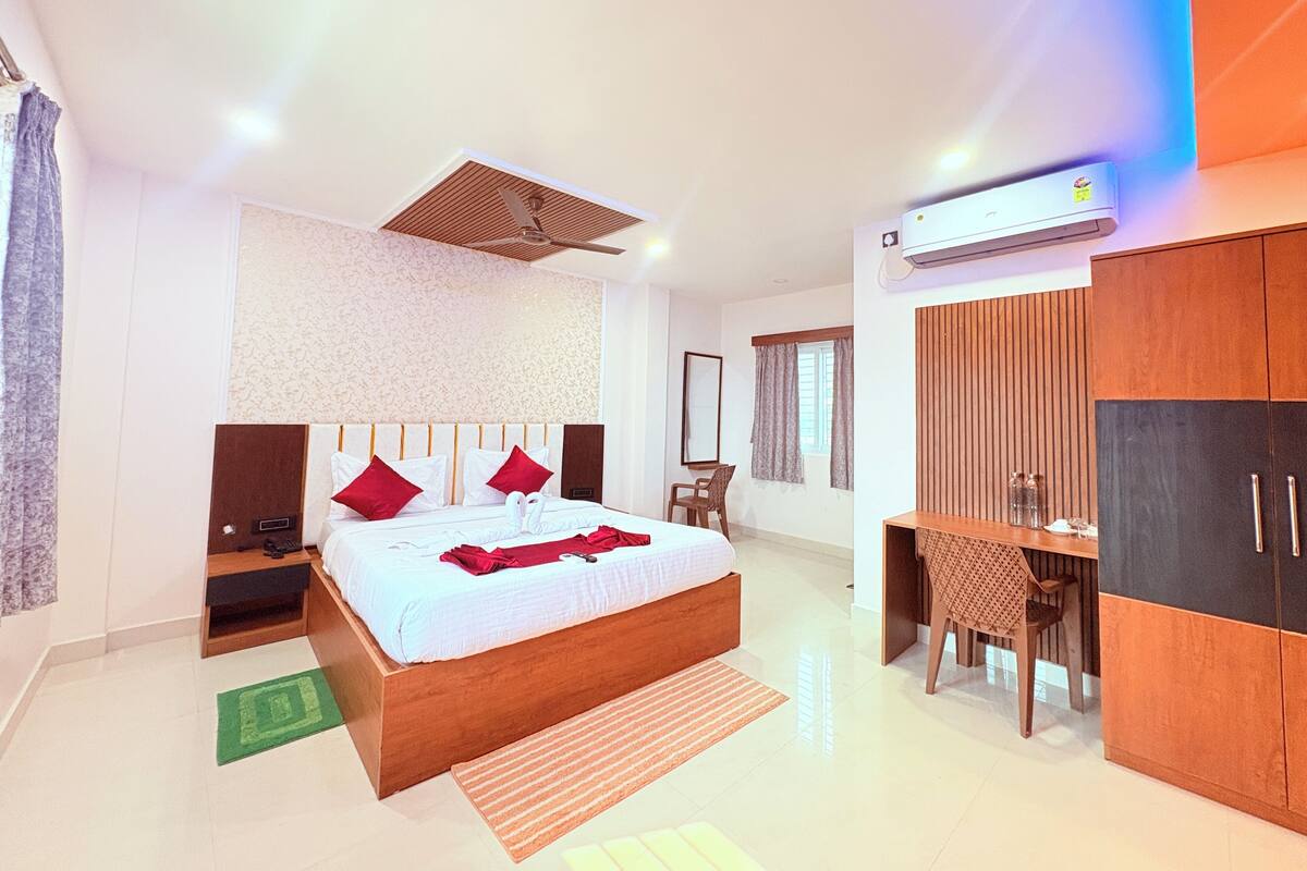 A modern hotel room with a large bed, a desk, and an air conditioning unit.