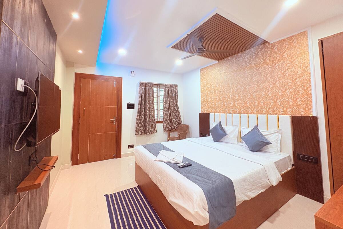 A hotel room with a large bed, a wooden wardrobe, a ceiling fan, and a window with curtains.