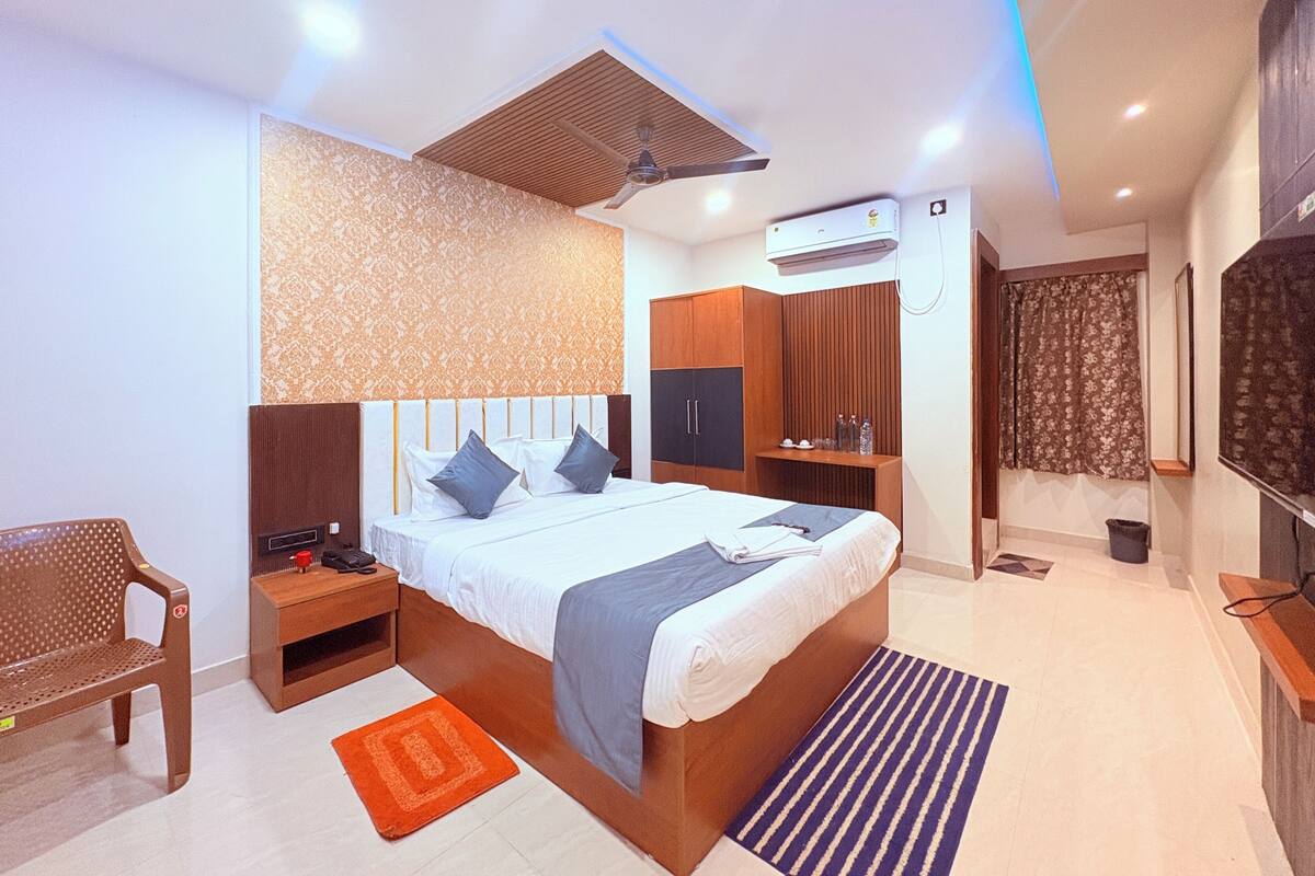 A modern hotel room with a bed, nightstands, a wardrobe, an air conditioning unit, a television, and a patterned wall.