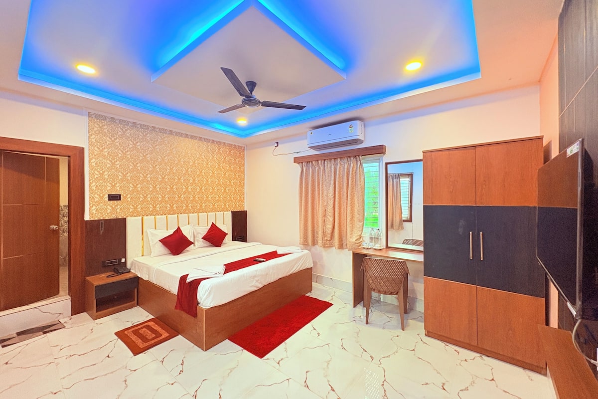 A hotel room with a bed, desk, wardrobe, ceiling fan, and a ceiling with blue lighting.