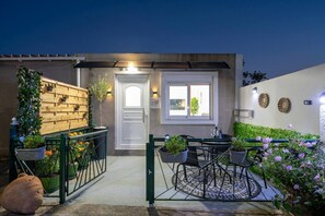 Et moderne hus med en lukket indkørsel, en lille terrasse med bord og stole, samt en have med blomster og beplantning.