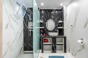 Uma casa de banho moderna com chuveiro em cabine de vidro, um espelho redondo, uma pia branca e um kit de primeiros socorros vermelho.