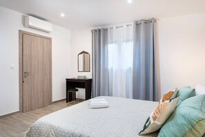 Quarto com cama, escrivaninha, espelho e janela com cortinas.